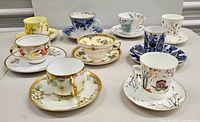 Nine assorted vintage teacups and saucers with varied floral and decorative patterns on a white surface