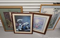 Four framed wall art pieces arranged leaning against a corrugated metal backdrop, showing various floral and natural themes