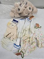 Image showing multiple pairs of new gardening gloves in floral and striped designs along with a pack of beige elastic bandage rolls wrapped together.