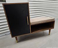 Retro-style wooden entry bench with side cabinet, black door panel, beige seat cushion, and brass details shown from front angle.