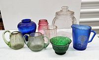 Photo of all glass and porcelain items arranged showing colors and variety, including blue Shirley Temple pitcher, green creamers, and other glass pieces.