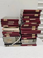 Stacked maroon and gray plastic film reel storage cases with assorted handwritten labels describing contents, including historical society-related films.