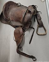 Side view of vintage Western saddle showing dark brown worn leather, embossed decorative patterns, stirrup and buckle.