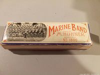 Top view of original Marine Band box showing branding, model number 1896, and a vintage illustration of the US Marine Band in black and white on top of the box.