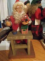 Front view of the 20 inch animated Santa seated on a wooden stool holding a toy house and hammer, showing condition and detail of the figure and base.