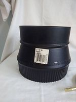 Black metal chimney pipe reducer with sticker label showing size 7" to 6" BW.