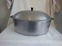Front view of vintage oval cast aluminum Dutch oven with lid on. The lid has a broken top handle.