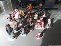 Multiple vintage Christmas village people figurines arranged on a floor surface, showing a variety of characters in winter attire and holding seasonal props.