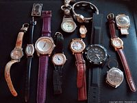 Photo capturing full set of 12 watches including wristwatches and one pocket watch arranged on black surface.