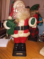 Photo of one Mr Claus figurine with candy cane and green sack standing on a black base labeled NOEL on a table