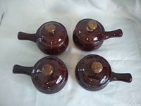 Top view of four dark brown ceramic soup bowls with lids, laid on white cloth background.