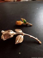 Close up of gold tone rose brooch with detailed petals and two leaves on curved stem