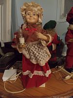 Mrs. Claus figure wearing a ruffled bonnet, glasses, red dress with white apron, holding a candle, showing cords and base where figure is loose from stand