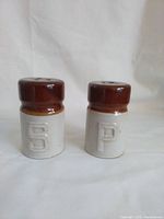 Salt and pepper shakers with brown tops and cream bottoms, embossed with letters 'S' and 'P'.
