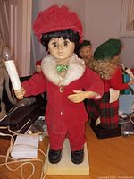 Front view of vintage animated boy Christmas caroler, dressed in red velvet with white fur trim, holding candle light.
