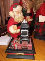 Photo of vintage Holiday Creations 1993 Santa musical scene showing Santa beside a black wood burning stove on a brick base with gift boxes and a NOEL plaque
