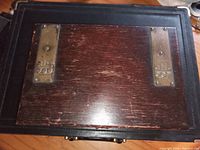 Closed view of antique wooden writer's box showing brass plates with rose-design and wooden exterior with scratches.