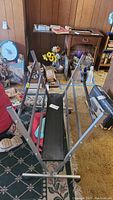 Metal art rack frame, angled view showing frame and wheels, surrounded by household items in a room with wood paneling.