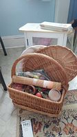 Wicker basket filled with decorative items including a rolled bamboo mat, green and white checkered cloth, various small decorative pieces