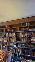Six shelves filled with a large and diverse collection of mostly hardcover books displayed on wooden shelving units against paneled wall.
