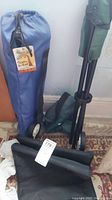 Blue camp chair bag with tag showing Paradise Bay Club brand, rolled folded chair and wheeled blue bag for stool.