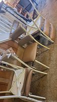 Photo showing four stacked vintage metal and vinyl dining chairs with cream-colored metal frames and light brown vinyl seats and backs.