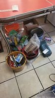 Photo of multiple cleaning buckets and assorted items including tins, packaged boxes, and tools clustered under a table.