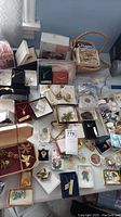 Overview of assorted costume jewelry on table, multiple boxed and loose pieces visible including necklaces, brooches, earrings, and rings.