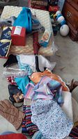 Photo showing a V-shaped cream foam rest on top of a pile of various household and clothing items including an umbrella with a red handle, several shirts in bright colors and patterns, and a handbag.