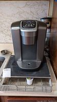 Front view of Keurig coffee maker on black stand with metal pull-out drawer for storing coffee pods underneath it.