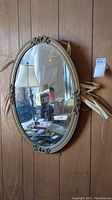 Front view of the oval-shaped plastic mirror hanging on a wood-paneled wall with visible scratches on the mirror surface and some dirt.