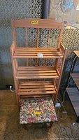Front view of wooden folding shelf rack with three shelves and floral footstool below.