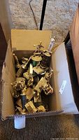 Box of assorted trophies showing different designs and finishes, some copper/gold colored, some with bases, all stored in a cardboard box needing cleaning.