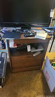 Wooden TV stand showing top surface with TV, electronic devices, papers, and cords. The wood finish appears worn with scratches and scuffs.