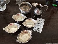 Overall grouping of creamer, sugar bowl and four salt cellars on wood surface
