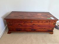 Front view of wooden chest showing reddish-brown wood with metal lock and hinges.