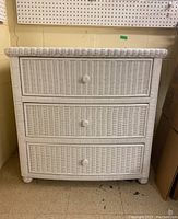 Front view of the white painted wicker dresser showing three drawers with wicker knobs.
