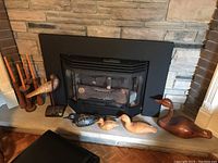 Four wooden duck figurines and three wooden candlestick holders arranged on hearth