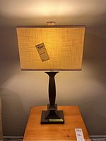 Front view of the lamp showing the rectangular fabric shade and resin base on a wooden table, lit to show warm light.