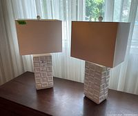 Pair of ceramic table lamps with rectangular bases featuring raised geometric square and rectangle pattern, each with a rectangular off-white fabric shade.