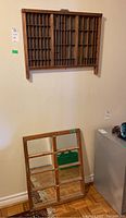 Wooden framed mirror with window pane style divided into nine rectangular sections, leaning against the wall below the shelf.
