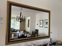 Front view of large rectangular mirror hanging on the wall, reflecting a dining room and chandelier.