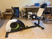 Side view of Advantage Fitness recumbent exercise bike in finished basement with various paint cans and boxes in background.