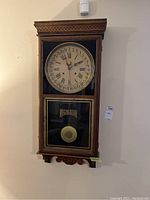 Full view of the vintage regulator wall clock mounted on the wall, showing its rectangular wooden frame and glass panel with pendulum.