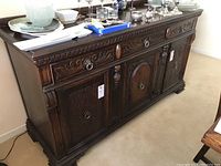 Left front angled view of antique wood sideboard showing carved details and contents on top