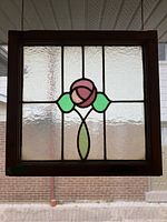 Full view of the stained glass panel showing the square design with a central pink rose and green leaves, framed in dark wood.
