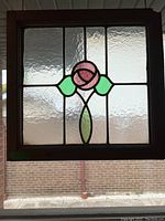 Vintage stained glass window panel hanging, showing central rose design with textured clear glass.