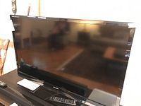 Photo showing full front view of Sharp Aquos 46-inch LCD TV with remote on stand