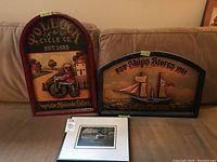 View of two vintage style wood plaques and one framed signed print arranged on a sofa.