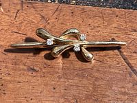 Front view of stylized gold bow brooch with four diamonds on wooden surface